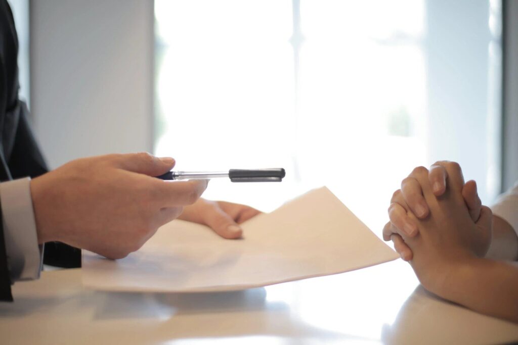 A person offers a pen and the mortgage application papers to another.